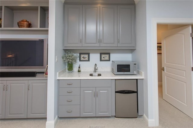 bar featuring gray cabinetry, stainless steel fridge, sink, and light carpet