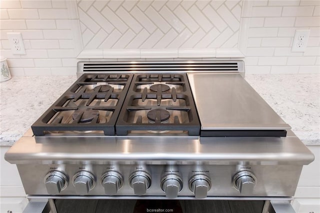 interior details featuring light stone counters, backsplash, and gas range