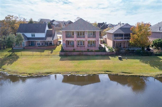 back of house featuring a water view, a balcony, and a lawn