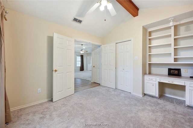 unfurnished bedroom featuring ceiling fan, lofted ceiling with beams, built in desk, and light carpet