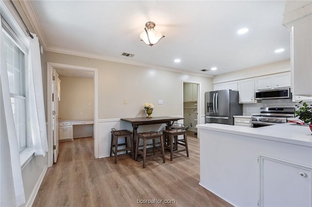 kitchen featuring white cabinetry, stainless steel appliances, ornamental molding, backsplash, and light wood-type flooring