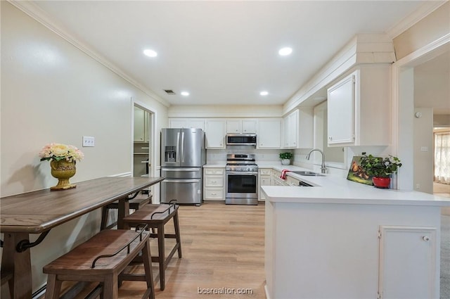 kitchen featuring kitchen peninsula, appliances with stainless steel finishes, crown molding, white cabinets, and light hardwood / wood-style floors