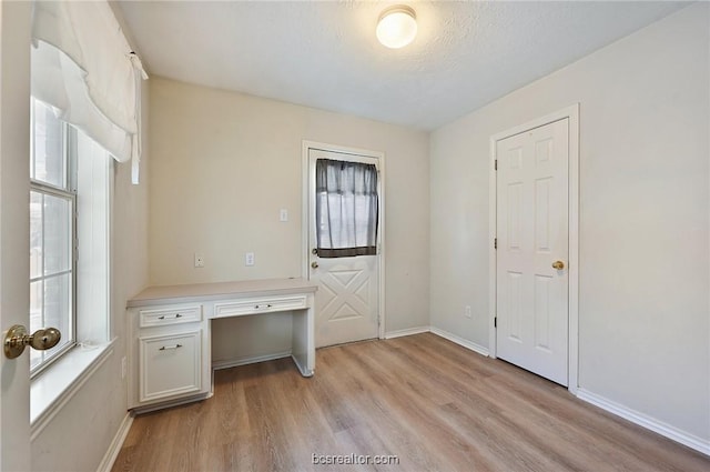 unfurnished office with a wealth of natural light, built in desk, a textured ceiling, and light wood-type flooring