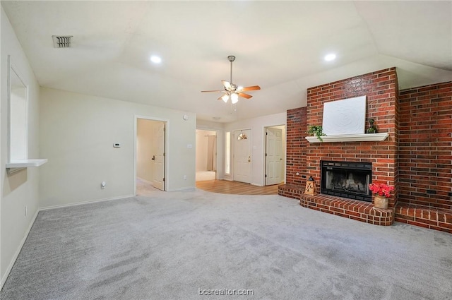 unfurnished living room featuring a brick fireplace, vaulted ceiling, ceiling fan, carpet floors, and brick wall