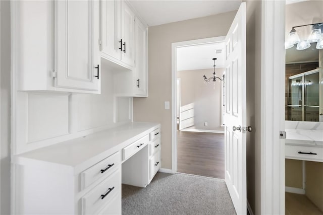 interior space with a notable chandelier, decorative light fixtures, light colored carpet, built in desk, and white cabinets