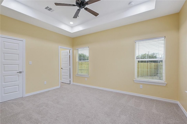 unfurnished room featuring ceiling fan, light colored carpet, a raised ceiling, and a healthy amount of sunlight