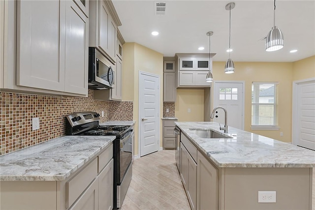 kitchen with sink, appliances with stainless steel finishes, a center island with sink, decorative light fixtures, and light wood-type flooring