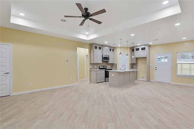 kitchen featuring stainless steel appliances, a center island with sink, decorative light fixtures, a raised ceiling, and light wood-type flooring