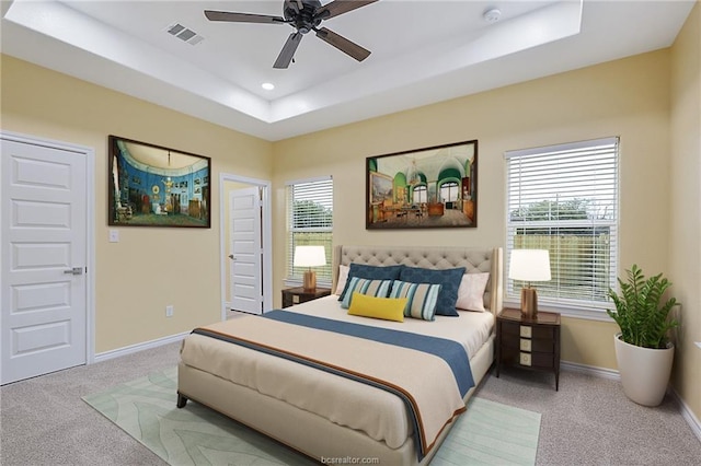 bedroom with a raised ceiling, light carpet, ceiling fan, and multiple windows