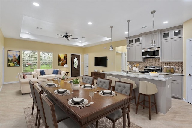 dining room with light hardwood / wood-style floors, sink, ceiling fan, and a tray ceiling