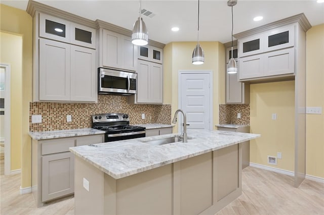 kitchen with sink, appliances with stainless steel finishes, light stone counters, an island with sink, and decorative light fixtures