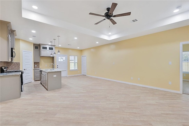 kitchen featuring appliances with stainless steel finishes, a kitchen island with sink, backsplash, decorative light fixtures, and light wood-type flooring