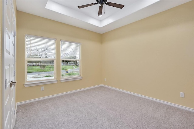 empty room with light carpet, ceiling fan, and a tray ceiling