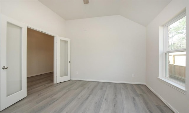 spare room with plenty of natural light, light hardwood / wood-style flooring, vaulted ceiling, and french doors