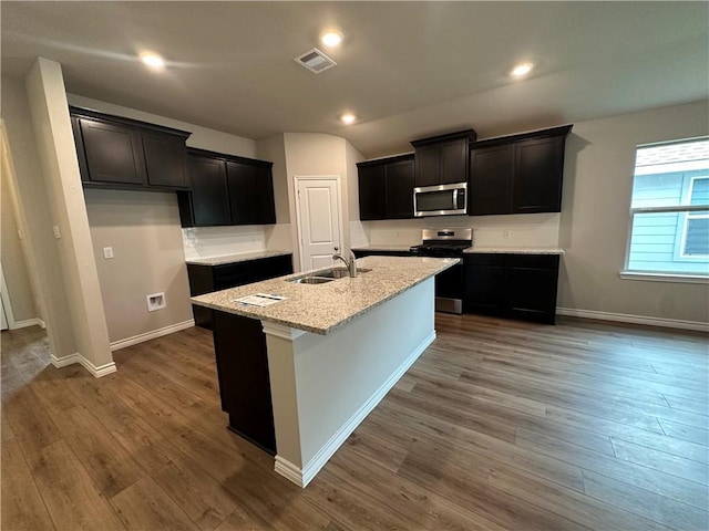 kitchen featuring appliances with stainless steel finishes, dark hardwood / wood-style flooring, light stone counters, a kitchen island with sink, and sink