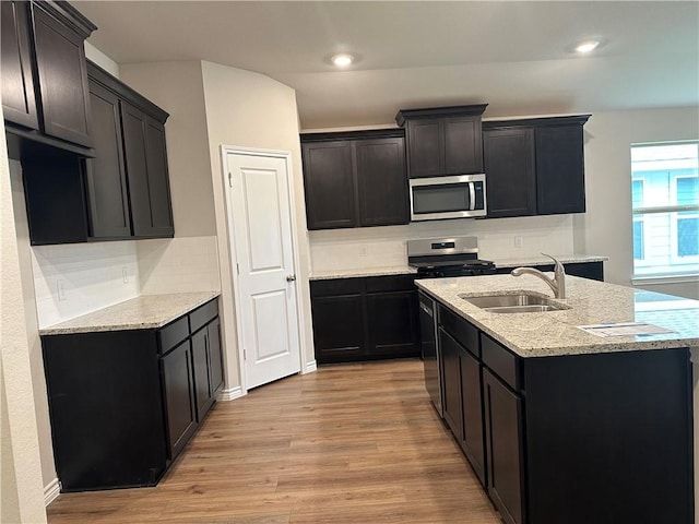 kitchen featuring light stone countertops, backsplash, stainless steel appliances, sink, and light hardwood / wood-style flooring