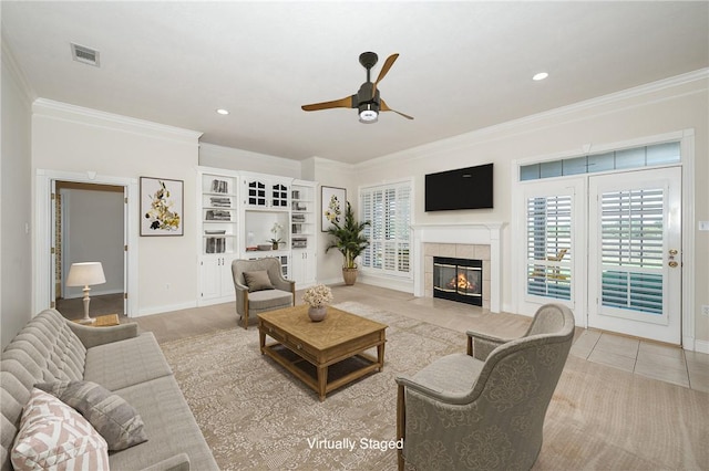 living room with a tiled fireplace, ceiling fan, light tile patterned flooring, and ornamental molding