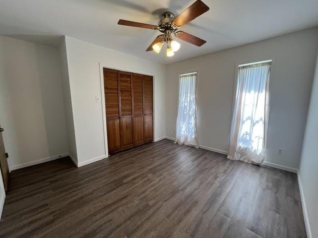 unfurnished bedroom with ceiling fan, dark wood-type flooring, a closet, and baseboards