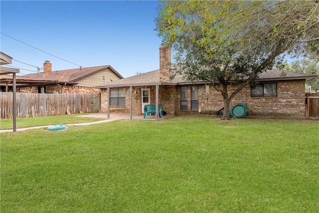 rear view of property with brick siding, a yard, a chimney, a patio area, and fence