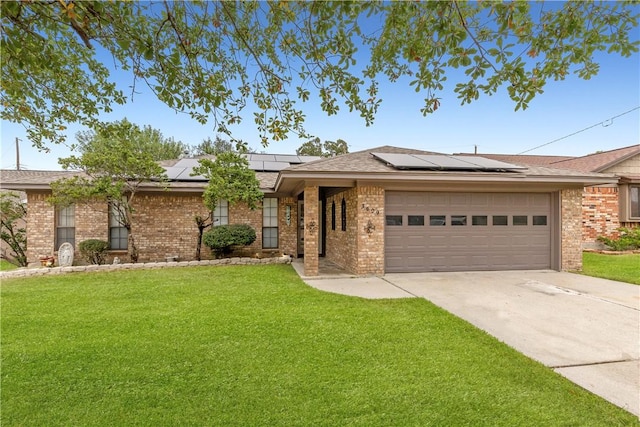 ranch-style home featuring brick siding, solar panels, concrete driveway, an attached garage, and a front yard