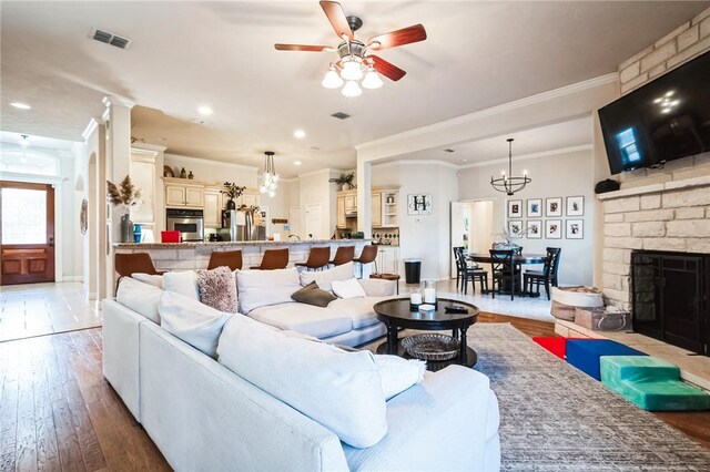 living area with a stone fireplace, ceiling fan with notable chandelier, light wood-style floors, and visible vents