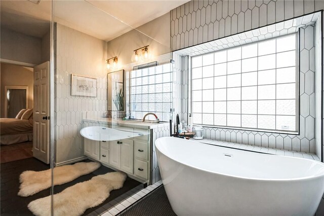 ensuite bathroom with ensuite bathroom, tile walls, tile patterned flooring, a freestanding bath, and vanity