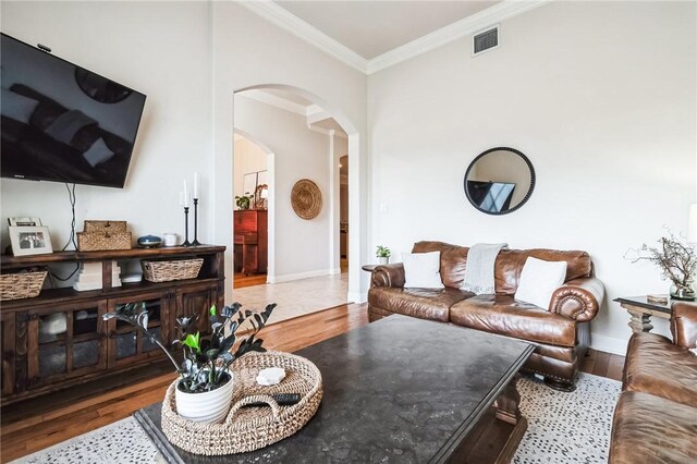 living area with arched walkways, visible vents, ornamental molding, and wood finished floors