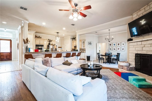 living room with a stone fireplace, light wood-style flooring, ceiling fan with notable chandelier, and visible vents