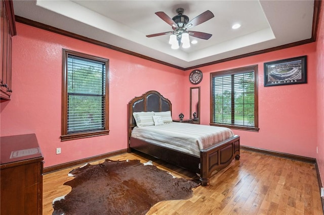 bedroom featuring light wood finished floors, multiple windows, and a raised ceiling