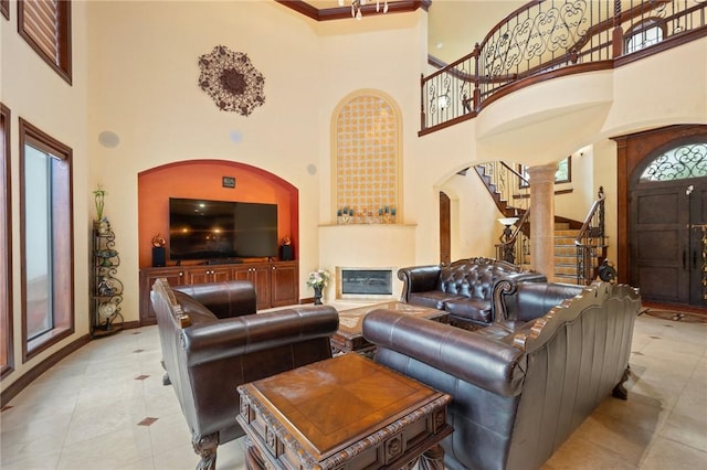 living area with stairs, a towering ceiling, tile patterned flooring, arched walkways, and a glass covered fireplace