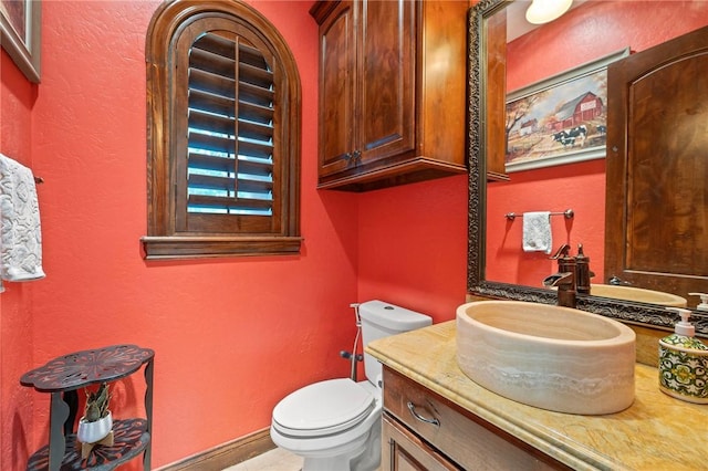 bathroom featuring vanity, toilet, a textured wall, and baseboards