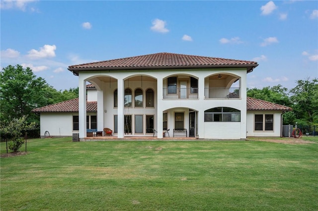 back of property with a tile roof, a balcony, cooling unit, and a lawn