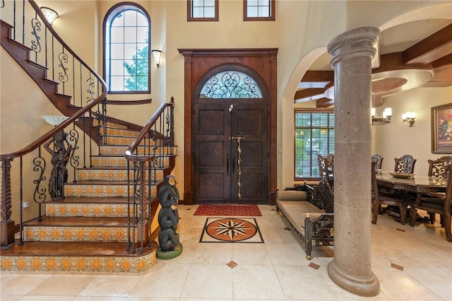 tiled entrance foyer with a healthy amount of sunlight, decorative columns, arched walkways, and stairs