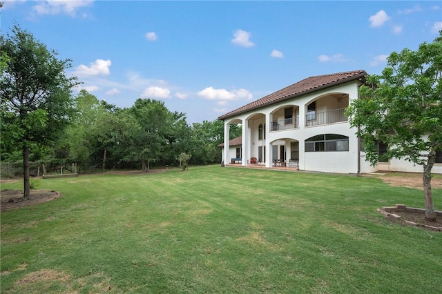 back of house featuring a yard, stucco siding, a tiled roof, and a balcony