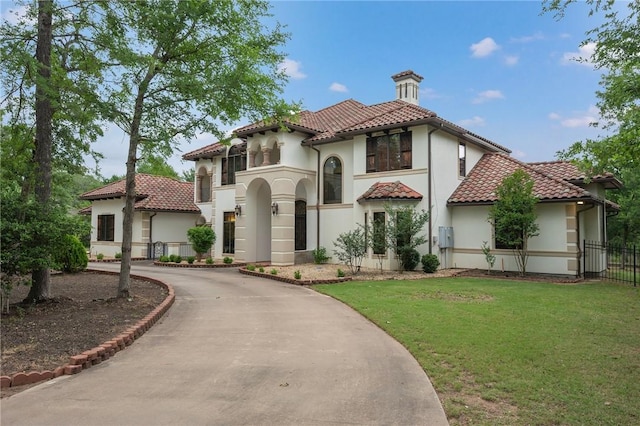 mediterranean / spanish home with stucco siding, a tile roof, fence, curved driveway, and a front yard