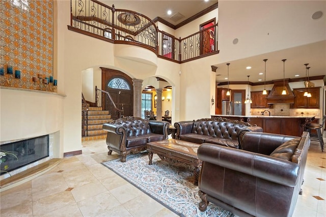 living area with ornate columns, stairway, crown molding, arched walkways, and a high ceiling