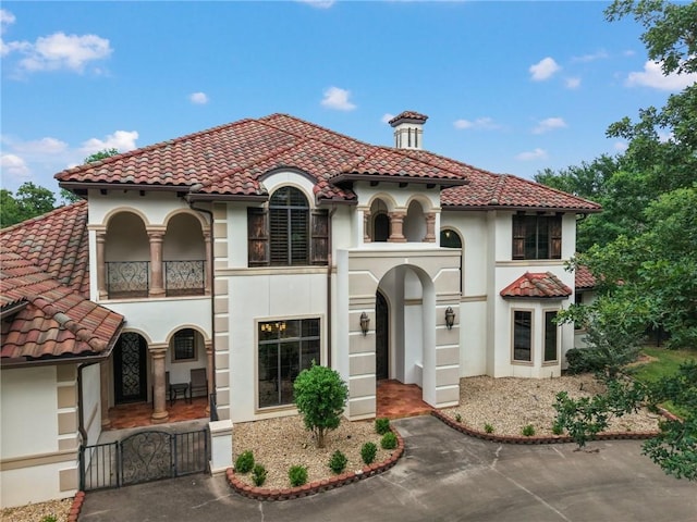 mediterranean / spanish-style house featuring a gate, a tile roof, stucco siding, and a balcony