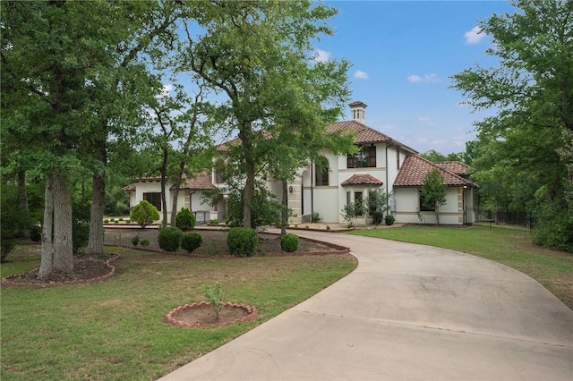 mediterranean / spanish home with a tiled roof, stucco siding, fence, curved driveway, and a front lawn