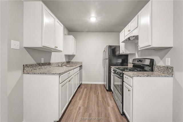 kitchen with light stone countertops, appliances with stainless steel finishes, white cabinets, and light hardwood / wood-style flooring