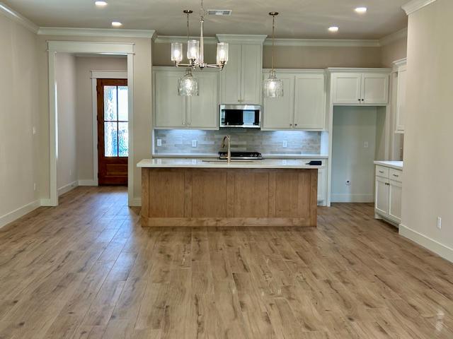 kitchen featuring white cabinetry, sink, pendant lighting, a kitchen island with sink, and light wood-type flooring