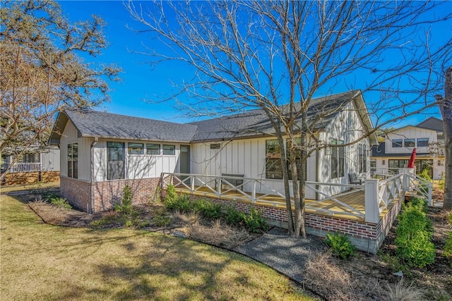 view of front facade featuring brick siding, board and batten siding, a front lawn, and roof with shingles