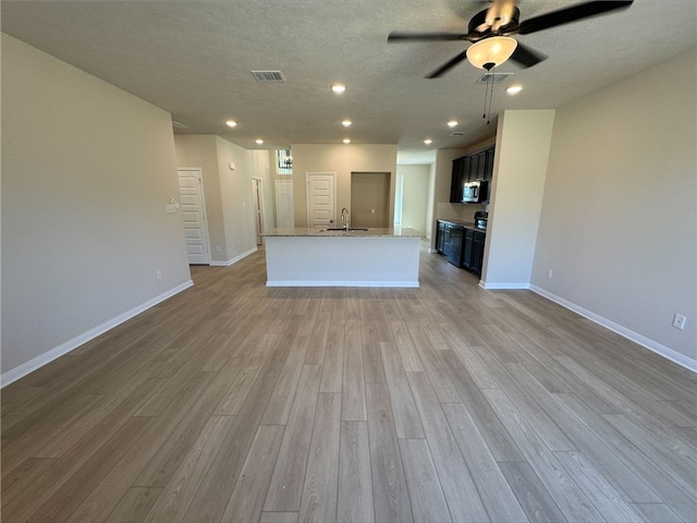 unfurnished living room featuring ceiling fan, sink, a textured ceiling, and light wood-type flooring