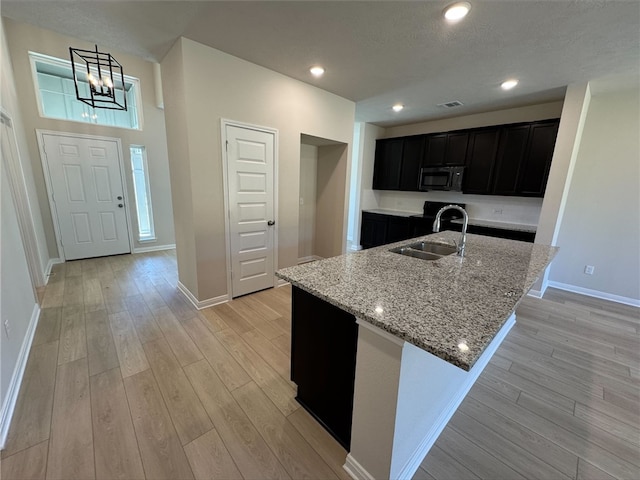 kitchen featuring an inviting chandelier, a center island with sink, sink, light stone countertops, and light hardwood / wood-style floors