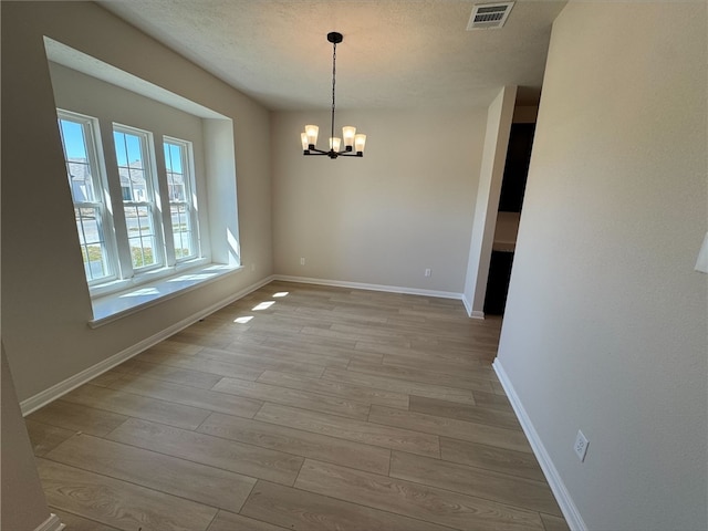 unfurnished dining area with light hardwood / wood-style floors, a textured ceiling, and an inviting chandelier