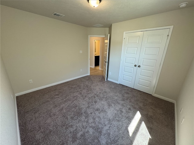 unfurnished bedroom featuring dark colored carpet, a textured ceiling, and a closet