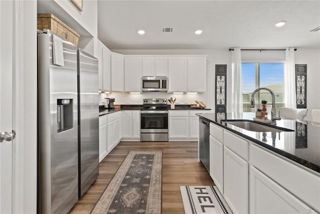 1988 Chief St, Bryan, TX 77807 - kitchen with appliances with stainless steel finishes, a sink, white cabinets, wood finished floors, and recessed lighting