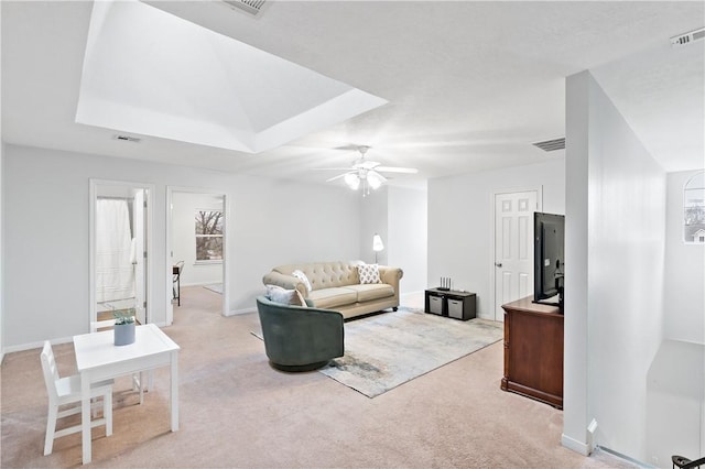 living room with a raised ceiling, light colored carpet, and ceiling fan