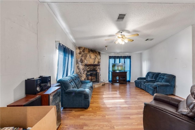 living room with a stone fireplace, ceiling fan, wood-type flooring, and a textured ceiling