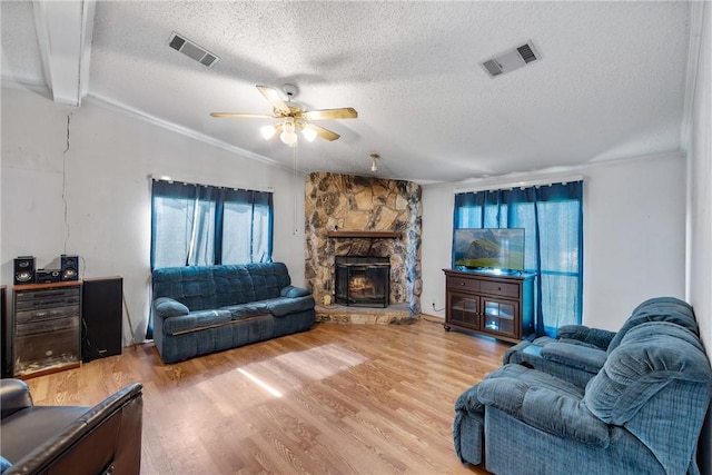 living room featuring ornamental molding, a textured ceiling, ceiling fan, hardwood / wood-style floors, and a stone fireplace