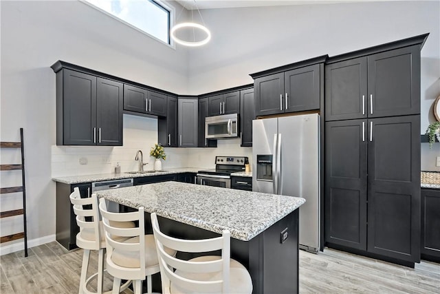 kitchen featuring dark cabinets, stainless steel appliances, a breakfast bar, a sink, and light stone countertops